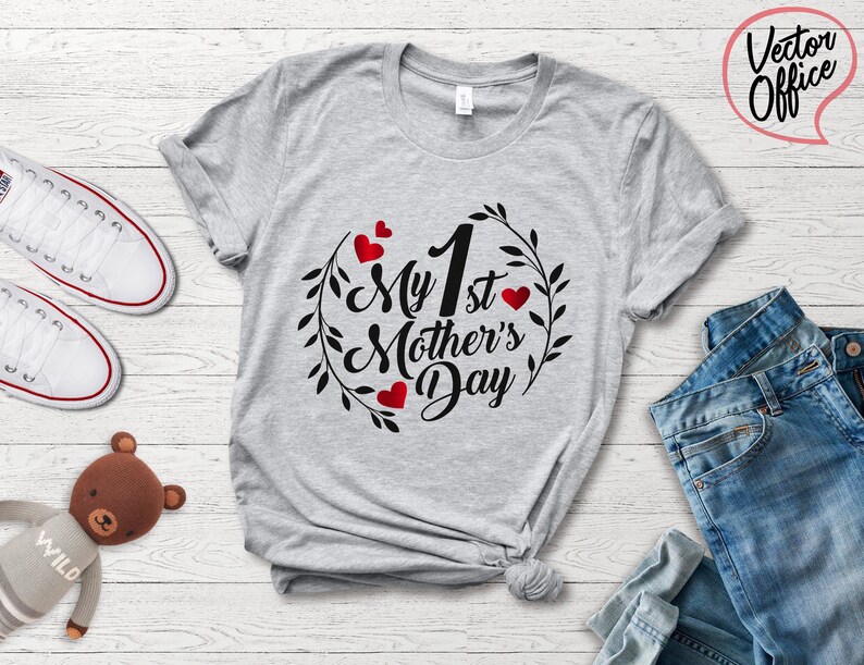 May include: Gray t-shirt with the text "My 1st Mother's Day" in black lettering with a wreath of leaves and red hearts around the text.