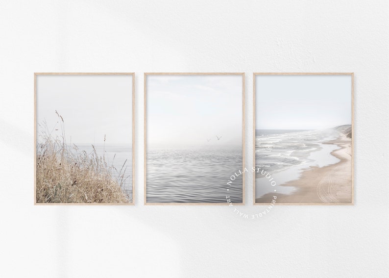 Puede incluir: Conjunto de tres impresiones enmarcadas que presentan escenas de playa minimalistas. La primera impresi&oacute;n muestra hierbas altas en primer plano con un oc&eacute;ano brumoso en el fondo. La segunda impresi&oacute;n muestra un oc&eacute;ano tranquilo con algunas aves volando por encima. La tercera impresi&oacute;n muestra una playa de arena con olas rompiendo en la costa.