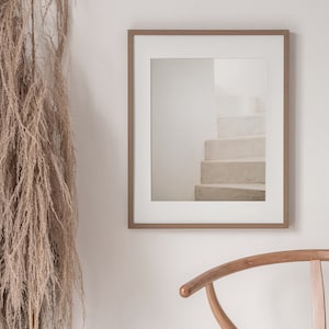 Peut inclure: Une photographie encadr&eacute;e d'un escalier blanc avec un cadre en bois brun clair. La photographie est accroch&eacute;e &agrave; un mur blanc &agrave; c&ocirc;t&eacute; d'une chaise en bois brun clair.