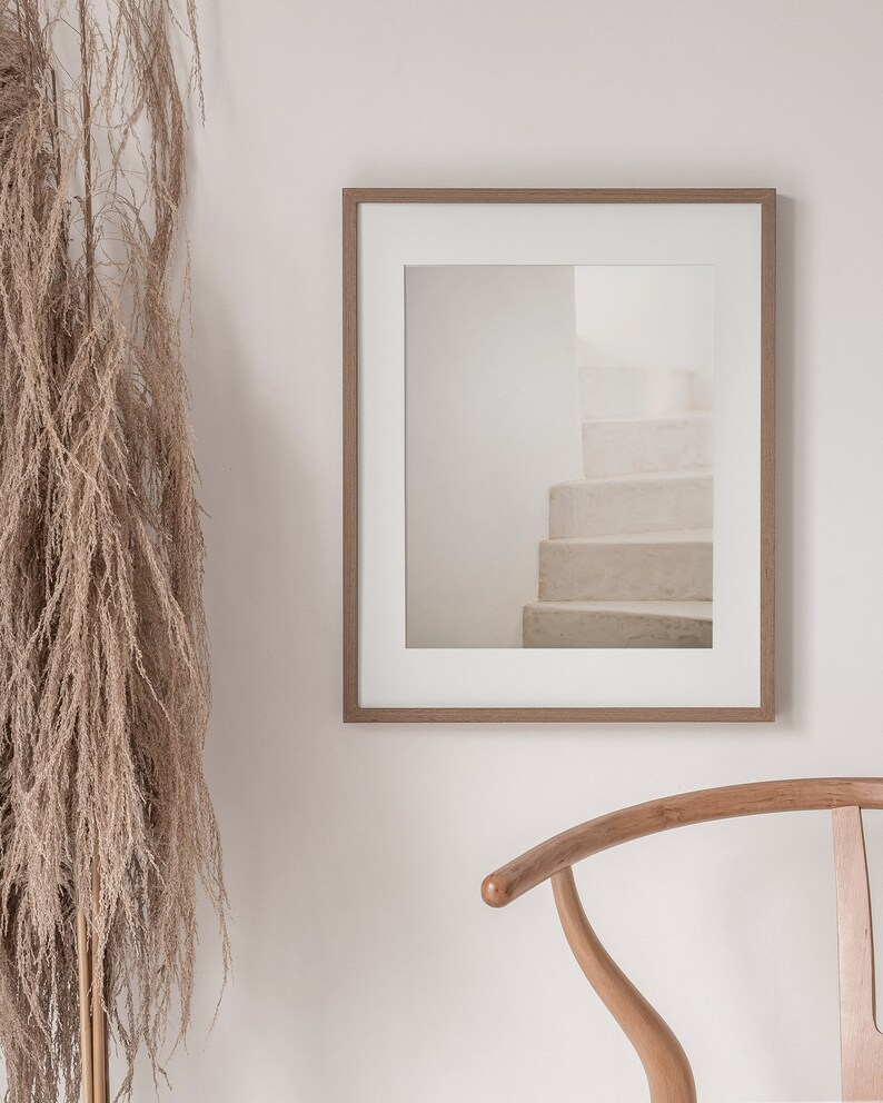 Peut inclure: Une photographie encadr&eacute;e d'un escalier blanc avec un cadre en bois brun clair. La photographie est accroch&eacute;e &agrave; un mur blanc &agrave; c&ocirc;t&eacute; d'une chaise en bois brun clair.