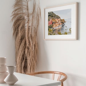 Pu&ograve; includere: Una fotografia incorniciata di una citt&agrave; costiera con edifici colorati su una collina che si affaccia sull'oceano. La foto &egrave; in una cornice di legno chiaro ed &egrave; appesa a un muro bianco.