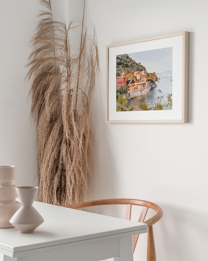 Pu&ograve; includere: Una fotografia incorniciata di una citt&agrave; costiera con edifici colorati su una collina che si affaccia sull'oceano. La foto &egrave; in una cornice di legno chiaro ed &egrave; appesa a un muro bianco.
