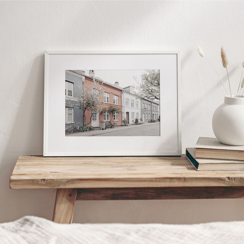 May include: A framed photograph of a row of colorful houses with white trim and a tree in the foreground. The houses are on a street with a sidewalk and a bicycle parked in front of one of the houses.