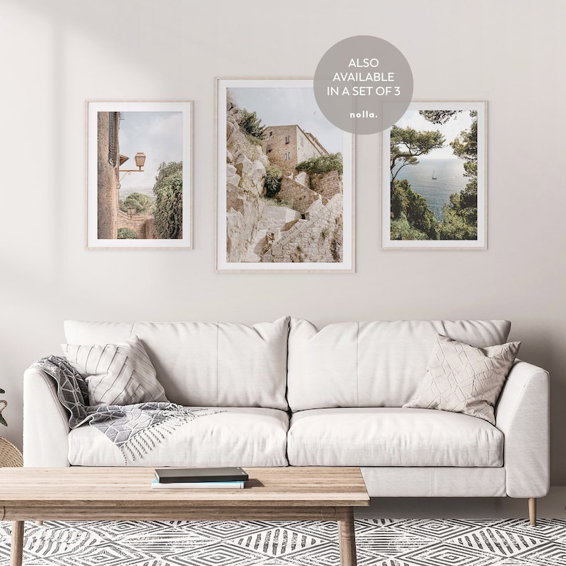 K&ouml;nnte beinhalten: Drei gerahmte Fotografien italienischer Landschaften. Das erste Foto zeigt ein Steinhaus mit einem Laternenpfahl im Vordergrund. Das zweite Foto zeigt einen Steinweg, der einen H&uuml;gel hinauf zu einem Geb&auml;ude f&uuml;hrt. Das dritte Foto zeigt einen Blick auf das Meer von einer Klippe mit B&auml;umen im Vordergrund. Der Text "ALSO AVAILABLE IN A SET OF 3" ist in der oberen rechten Ecke des Bildes sichtbar.