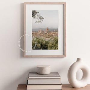 K&ouml;nnte beinhalten: Ein gerahmtes Foto einer Stadtlandschaft mit einem gro&szlig;en Kuppelgeb&auml;ude im Zentrum. Das Foto ist in einem hellen Holzrahmen und h&auml;ngt an einer wei&szlig;en Wand. Unter dem Foto stehen B&uuml;cher und eine Vase auf einem Holztisch.