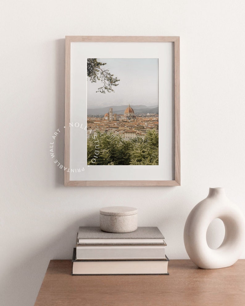 K&ouml;nnte beinhalten: Ein gerahmtes Foto einer Stadtlandschaft mit einem gro&szlig;en Kuppelgeb&auml;ude im Zentrum. Das Foto ist in einem hellen Holzrahmen und h&auml;ngt an einer wei&szlig;en Wand. Unter dem Foto stehen B&uuml;cher und eine Vase auf einem Holztisch.