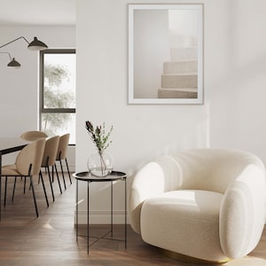 Peut inclure: Un fauteuil blanc moelleux avec une base dor&eacute;e se trouve dans un salon avec une table d'appoint noire et une estampe encadr&eacute;e d'un escalier blanc. Un vase avec un petit bouquet de fleurs se trouve sur la table.