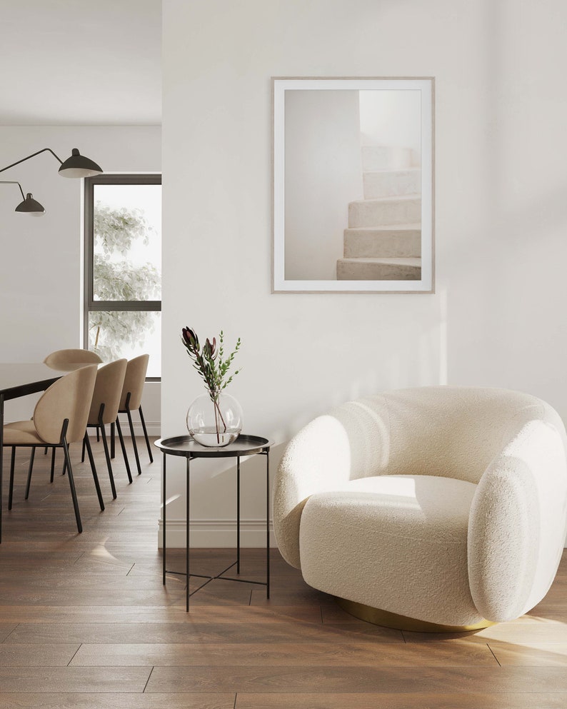 Peut inclure: Un fauteuil blanc moelleux avec une base dor&eacute;e se trouve dans un salon avec une table d'appoint noire et une estampe encadr&eacute;e d'un escalier blanc. Un vase avec un petit bouquet de fleurs se trouve sur la table.
