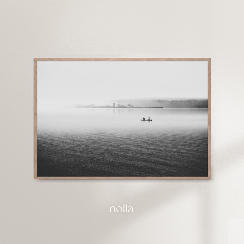 May include: A black and white photograph of a lake with a small boat in the distance. The lake is calm and the sky is overcast. The photo is framed in a wooden frame.