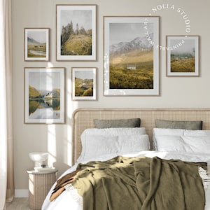 May include: Five framed landscape photographs of mountains, lakes, and fields in Scotland. The photos are hung on a light beige wall above a bed with a white duvet and a green throw blanket.