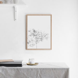 May include: A black and white line art print of a flower in a wooden frame. The print is hanging on a white wall above a table with a candle and books.