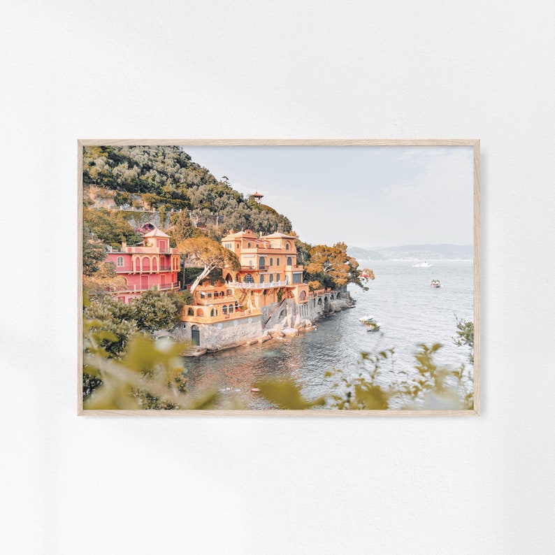 Pu&ograve; includere: Una fotografia di una villa italiana colorata su una scogliera che domina l'oceano. La villa &egrave; dipinta in tonalit&agrave; di giallo, arancione e rosa e ha un tetto in terracotta. L'oceano &egrave; di un blu profondo e il cielo &egrave; di un azzurro chiaro. Alberi e vegetazione verdeggianti circondano la villa.