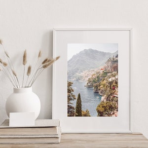 May include: A framed photograph of a coastal town nestled into a hillside overlooking a blue body of water. The town is surrounded by lush green trees and the water is dotted with boats.