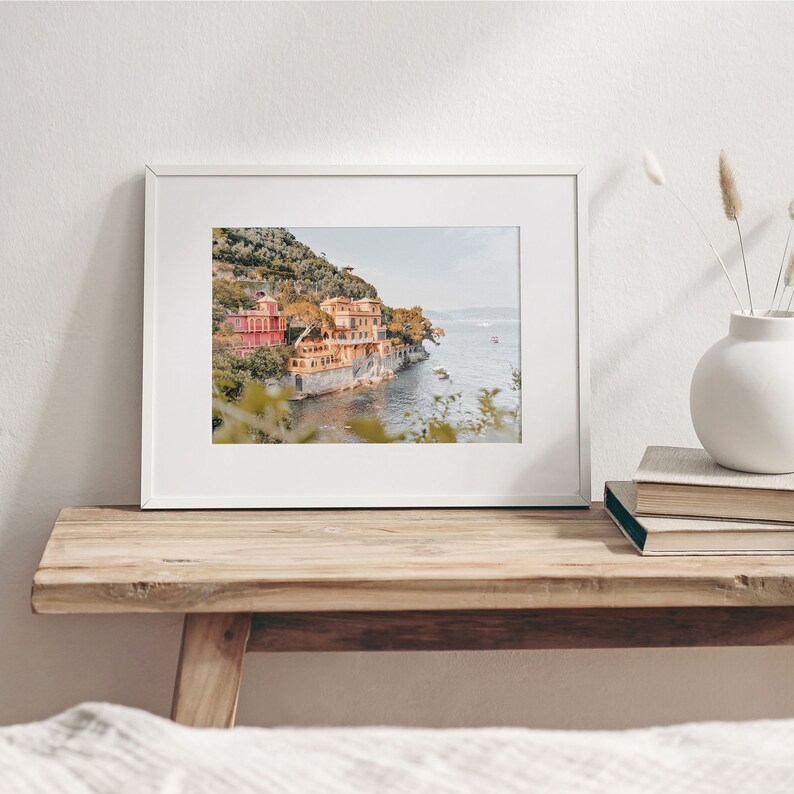 Pu&ograve; includere: Una fotografia incorniciata di una citt&agrave; costiera con edifici colorati su una collina che si affaccia sul mare. La foto &egrave; in una cornice bianca e si trova su un tavolo di legno.