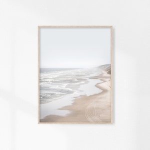 May include: A framed photograph of a sandy beach with waves crashing on the shore. The photo is taken from a high vantage point, showing the beach stretching out into the distance. The sky is a pale blue, and the water is a light turquoise.