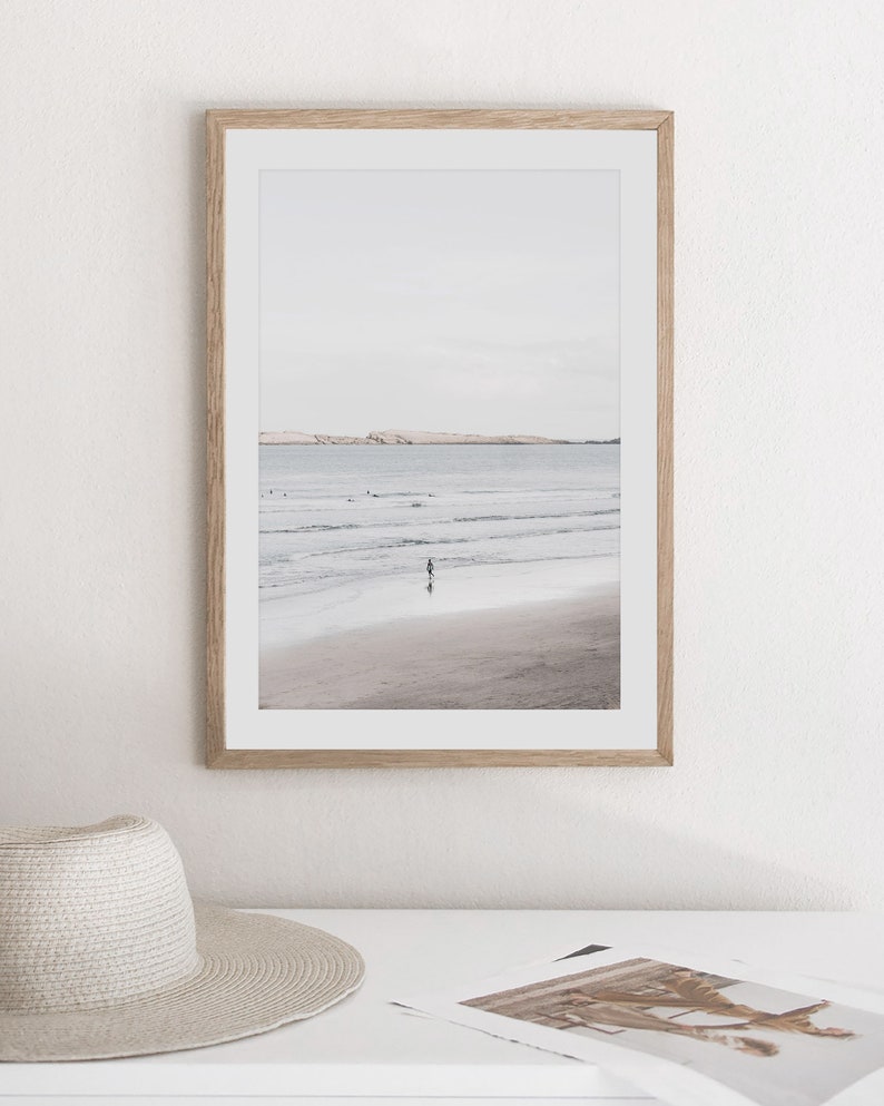 Puede incluir: Una fotograf&iacute;a enmarcada de una escena de playa con una persona caminando en el agua. La playa es arenosa y el agua es de color azul claro. El cielo es de color gris claro.