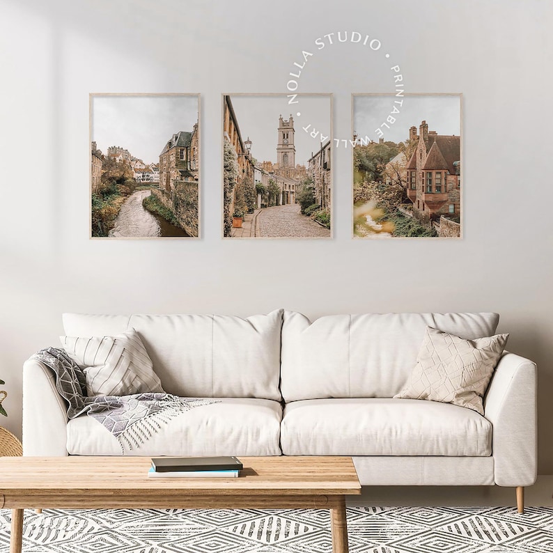 May include: Set of three framed prints featuring scenic views of a European city with cobblestone streets, stone buildings, and a church steeple. The prints are in a rustic style with a muted color palette.
