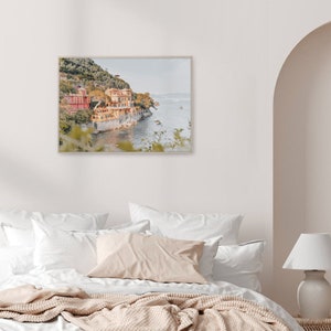 Pu&ograve; includere: Una fotografia incorniciata di una citt&agrave; costiera con edifici colorati su una collina che si affaccia sull'oceano. La foto &egrave; in una cornice di legno chiaro e appesa a una parete bianca.