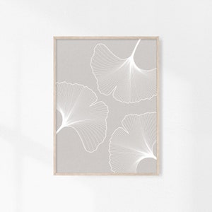 Puede incluir: Una impresi&oacute;n art&iacute;stica enmarcada con tres dise&ntilde;os de hojas de ginkgo blancas sobre un fondo gris claro. Las hojas presentan patrones de venas detallados y est&aacute;n enmarcadas en un marco de madera natural, creando una est&eacute;tica minimalista.