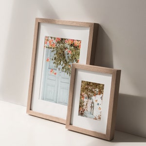 May include: Two wooden picture frames with white mats, one larger than the other, both displaying colorful photographs of a European city scene.