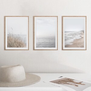 Puede incluir: Tres impresiones enmarcadas de paisajes marinos en un estilo minimalista. Las impresiones presentan una playa con olas, un paisaje marino con un p&aacute;jaro volando por encima y un primer plano de hierbas altas.