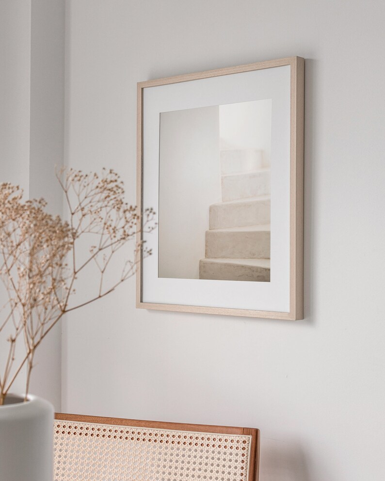 Peut inclure: Une photographie encadr&eacute;e d'un escalier blanc avec un cadre en bois clair. La photographie est accroch&eacute;e &agrave; un mur blanc.