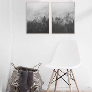 May include: Two black and white framed prints of a foggy forest scene. The prints are hanging on a white wall above a white chair with wooden legs.