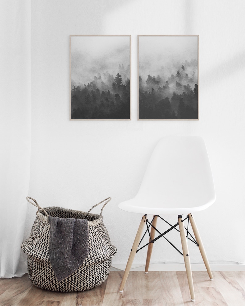 May include: Two black and white framed prints of a foggy forest scene. The prints are hanging on a white wall above a white chair with wooden legs.