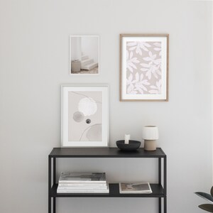 May include: Three framed prints on a white wall above a black metal shelf with books and a white ceramic candle holder. The prints are abstract art with circles and lines, a floral pattern, and a photograph of a white staircase.