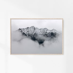 May include: A black and white photograph of a mountain range partially obscured by clouds. The mountain peaks are covered in snow.