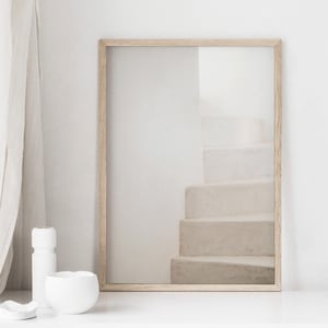 Peut inclure: Une photographie encadr&eacute;e d'un escalier blanc avec un cadre en bois brun clair. La photographie est sur une surface blanche.