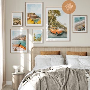 May include: A set of six framed prints featuring scenic views of the Italian coastline. The prints feature a variety of landscapes, including a colorful town, a winding road, a boat in the water, and a lush forest. The prints are all in a similar style, with a vintage, faded look. The prints are arranged in a grid on a wall above a bed with a white headboard and a gray blanket.