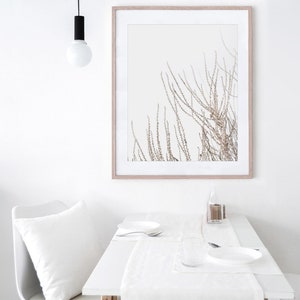 May include: A white table setting with a white tablecloth, a white plate, a white napkin, a clear glass, and a silver fork. A framed print of a brown branch with white background hangs on the wall above the table.