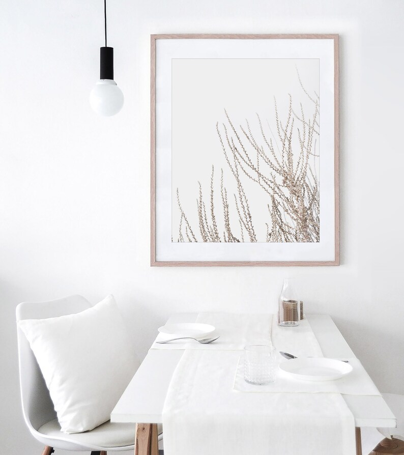 May include: A white table setting with a white tablecloth, a white plate, a white napkin, a clear glass, and a silver fork. A framed print of a brown branch with white background hangs on the wall above the table.