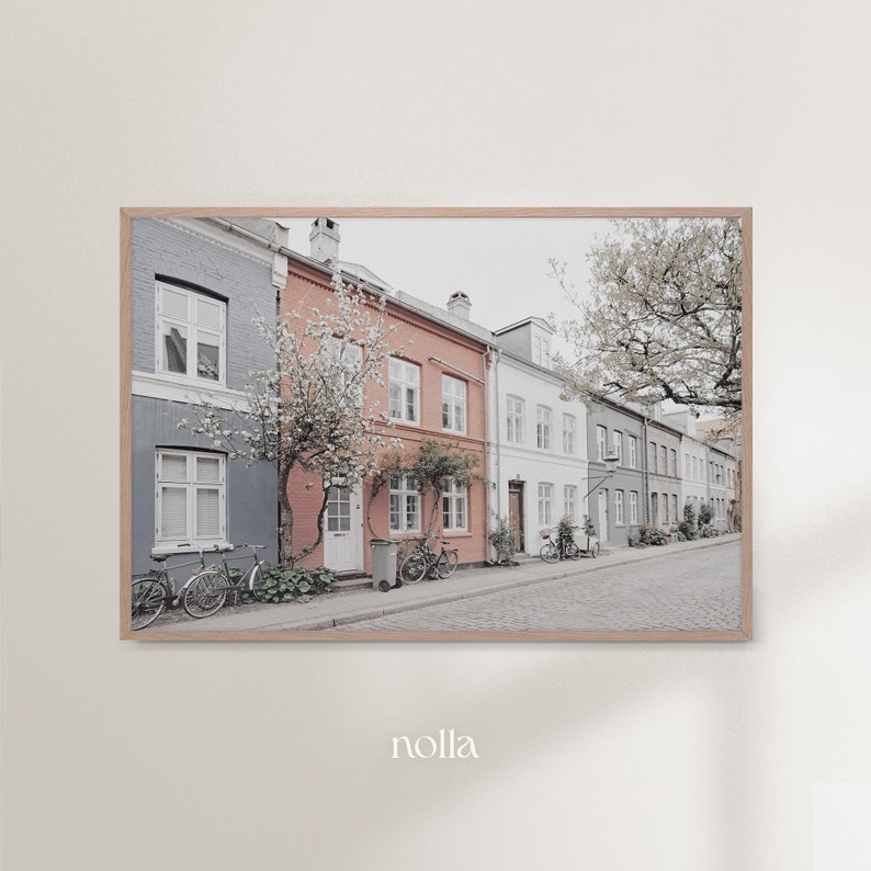 May include: A row of colorful houses with white trim and windows, lined with trees and bicycles parked in front. The houses are painted in shades of gray, pink, and white.