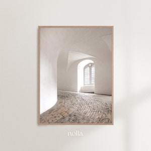 May include: A white room with a curved brick floor and a large arched window. The room is lit by natural light coming through the window.