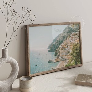 May include: A framed photograph of a coastal town with colorful buildings on a cliffside overlooking a blue ocean. The photo is in a rustic wooden frame.
