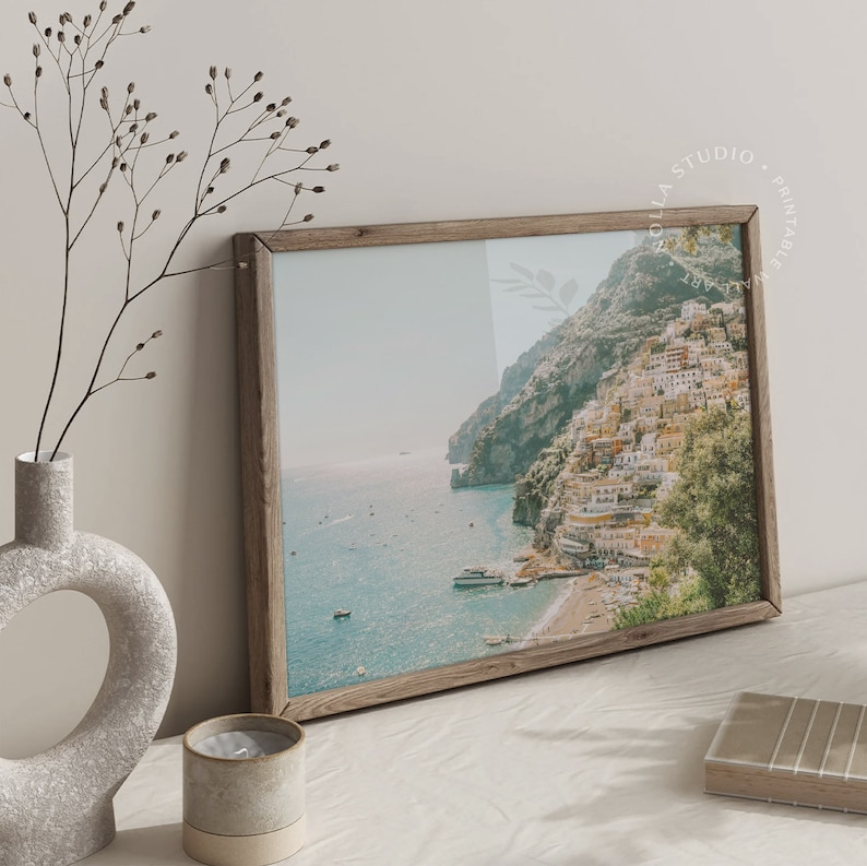 May include: A framed photograph of a coastal town with colorful buildings on a cliffside overlooking a blue ocean. The photo is in a rustic wooden frame.
