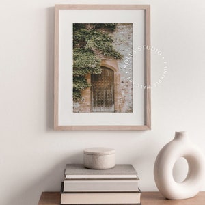 May include: A framed print of an old wooden door with ivy growing on the wall. The print is in a light wood frame and has a white mat. The print is titled "Nollas Studio. Printable Wall Art."