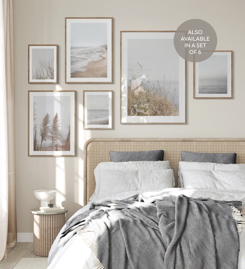 Puede incluir: Un dormitorio con una cama con una manta gris y almohadas blancas. Hay cinco impresiones enmarcadas en la pared sobre la cama. Las impresiones son todas de paisajes marinos y terrestres. El texto "ALSO AVAILABLE IN A SET OF 6" est&aacute; en la pared.