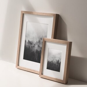 May include: Two framed black and white prints of a foggy forest landscape. The larger frame is on the left and the smaller frame is on the right.