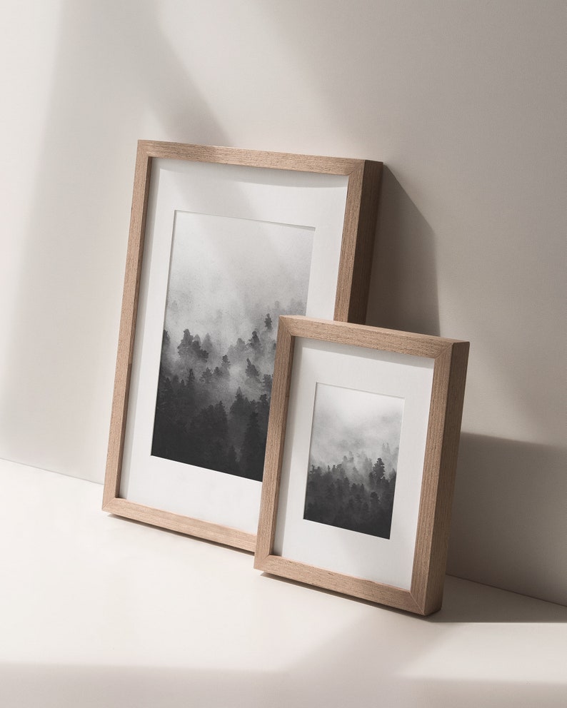 May include: Two framed black and white prints of a foggy forest landscape. The larger frame is on the left and the smaller frame is on the right.