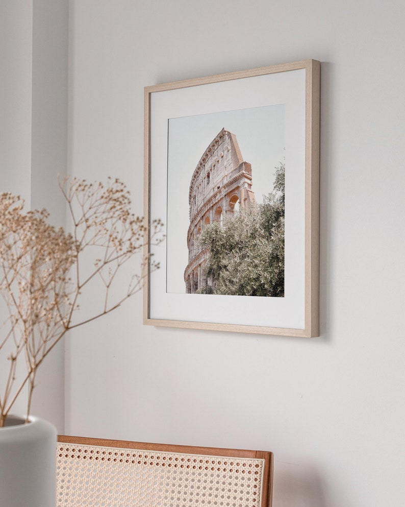May include: A framed photograph of the Colosseum in Rome, Italy. The photo is in a light wood frame and shows the Colosseum from a low angle, with trees in the foreground.