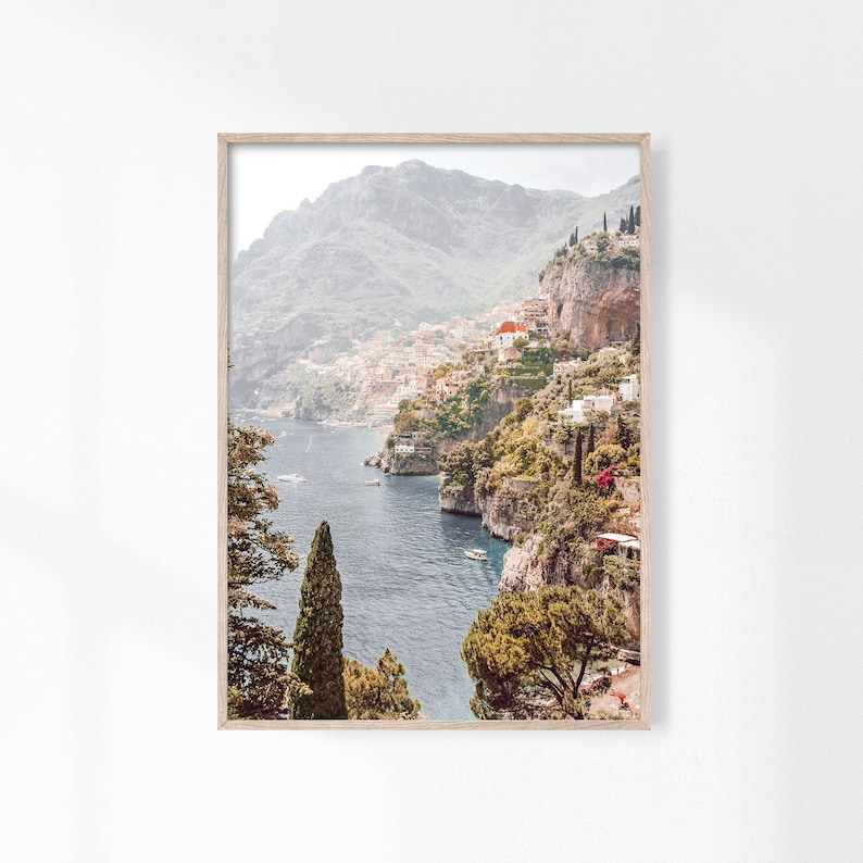 May include: A scenic photograph of a coastal town nestled between lush green cliffs and a sparkling blue sea. The town is built on the slopes of the cliffs, with white buildings and red roofs. The sea is calm and clear, with a few boats visible in the distance.