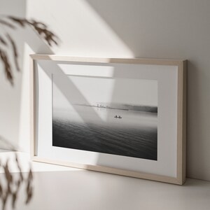 May include: A black and white photograph of a lake with a small boat in the distance. The photo is framed in a light wood frame.
