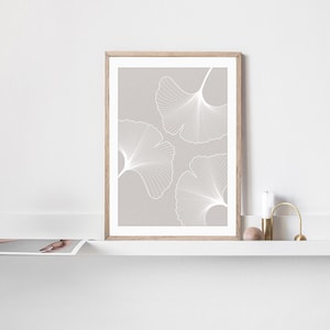 Puede incluir: Una impresi&oacute;n enmarcada con tres dise&ntilde;os de hojas de ginkgo blancas sobre un fondo gris claro. La obra de arte se muestra en un marco de madera clara. La impresi&oacute;n se exhibe en una estanter&iacute;a blanca con una vela y objetos decorativos.