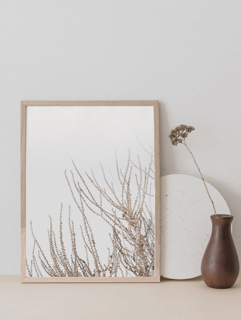 May include: A framed print of a minimalist botanical illustration featuring delicate brown branches against a white background. The print is displayed on a light beige surface with a round white coaster and a brown vase.
