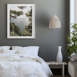 K&ouml;nnte beinhalten: Ein wei&szlig;es Bett mit einem wei&szlig;en Bettbezug und einer wei&szlig;en Wolldecke. Das Bett steht in einem Schlafzimmer mit einer grauen Wand, einem wei&szlig;en gerahmten Bild von einem Segelboot im Meer, einer wei&szlig;en H&auml;ngeleuchte aus Weidengeflecht und einer wei&szlig;en Vase auf einem wei&szlig;en Beistelltisch aus Weidengeflecht.