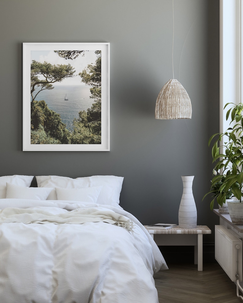K&ouml;nnte beinhalten: Ein wei&szlig;es Bett mit einem wei&szlig;en Bettbezug und einer wei&szlig;en Wolldecke. Das Bett steht in einem Schlafzimmer mit einer grauen Wand, einem wei&szlig;en gerahmten Bild von einem Segelboot im Meer, einer wei&szlig;en H&auml;ngeleuchte aus Weidengeflecht und einer wei&szlig;en Vase auf einem wei&szlig;en Beistelltisch aus Weidengeflecht.