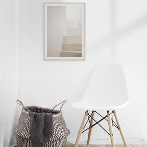 Peut inclure: Une chaise blanche avec des pieds en bois et un si&egrave;ge en osier noir se trouve devant un mur blanc avec une photographie encadr&eacute;e d'un escalier blanc. Un panier en osier noir et blanc se trouve sur le sol &agrave; c&ocirc;t&eacute; de la chaise.